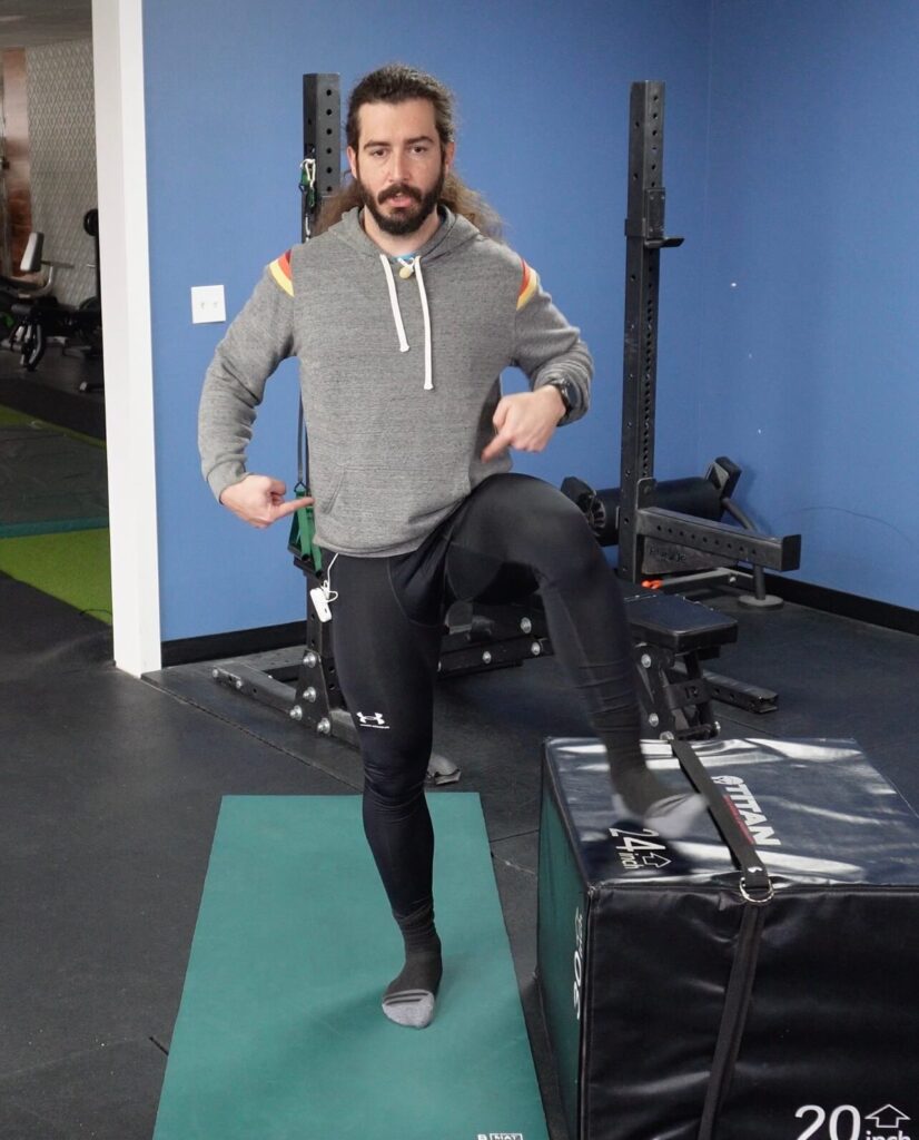 Dr. John demonstrating keeping his hips level while moving one leg over the box for the last exercise of the hip mobility routine